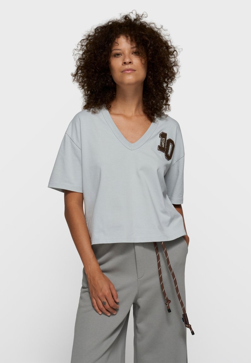 Camiseta de cuello en V de color azul claro, fabricada con tela suave, con un diseño corto y un detalle bordado con el número "10" en el pecho izquierdo.