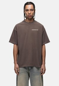 Bruine oversized t-shirt van zachte katoenstof met een ronde hals en korte mouwen; heeft "GOODFORNOTHING" in het wit op de borst gedrukt.