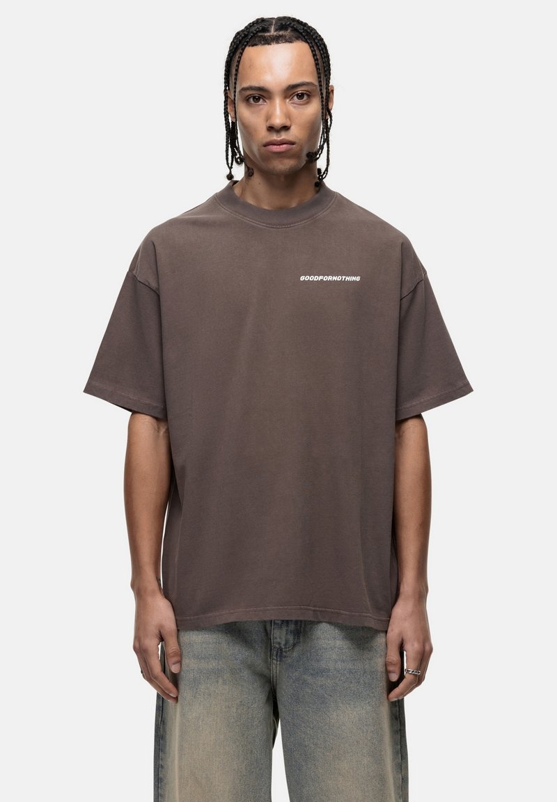 Bruine oversized t-shirt van zachte katoenstof met een ronde hals en korte mouwen; heeft "GOODFORNOTHING" in het wit op de borst gedrukt.
