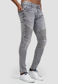 Jeans in denim grigio con dettagli a coste, vestibilità slim, cinque tasche e leggera scoloritura, abbinati a sneakers bianche.