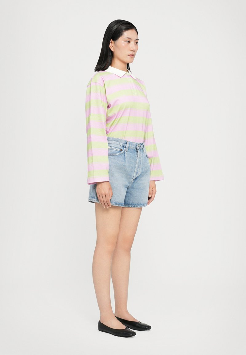 Polo à manches longues rayé rose et vert, associé à un short en jean bleu clair. Des chaussures noires à semelle plate complètent la tenue.