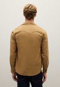Katoenen overhemd met lange mouwen in tanskleur met een puntige kraag en een gebogen onderkant. Voorzien van knoopmanchetten en een western yoke-detail aan de achterkant.