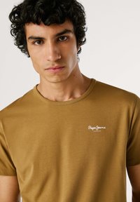 Hnedé bavlnené tričko s okrúhlym výstrihom, krátkymi rukávmi a bielym logom "Pepe Jeans London". Hladká textúra a priliehavý strih.