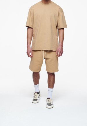 T-shirt en coton beige et short assorti avec taille élastique. Le t-shirt a un col rond et un léger détail sur la poitrine. Baskets robustes.