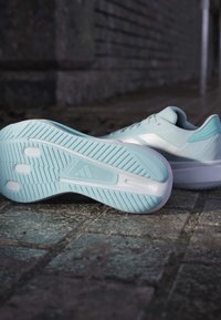 Hellblaue Sportschuhe mit einem strukturierten Obermaterial, weißen Akzenten und einer Gummiaußensohle, die ein einzigartiges Profil für besseren Halt aufweist.