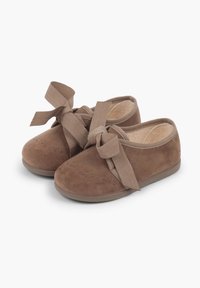 Brune ruskindsko med rund tå, der har en stor sløjfedeal foran og en fleksibel gummisål. Prikket design på tåområdet.