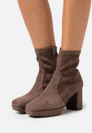 Brune ruskindsankelstøvler med spidse tåer, blokheel og lynlås i siden. Har en glat overflade og en tætsiddende ankelstil.