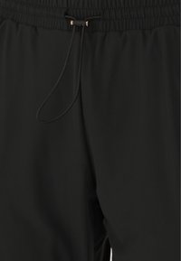 Svarta athletiska byxor med elastisk midja, med dragsko och slät, lättviktig tyg. Texturerad yta synlig.