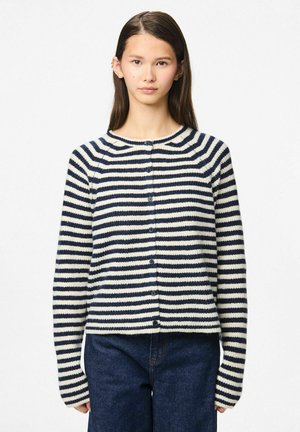 Cardigan a righe nei colori blu navy e crema; texture in maglia, scollatura rotonda e chiusura frontale con bottoni; maniche lunghe. Abbinato a jeans scuri.