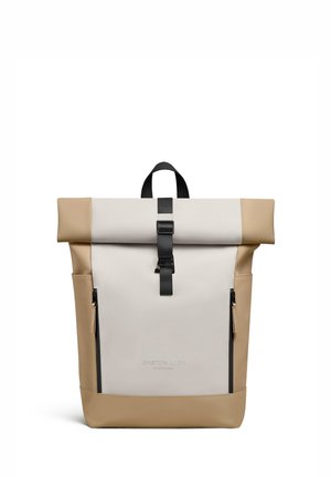 Beige en crèmekleurige rolltop-rugzak met zwarte gesp, twee verticale ritsen aan de voorkant en een handvat, merknaam "Gaston Luga Stockholm" gegraveerd aan de voorkant.