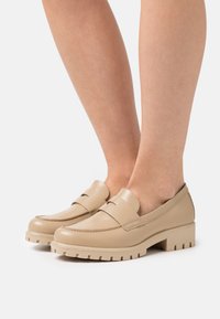 Mocassins en cuir beige avec un bout arrondi, une couture minimale et une semelle texturée, dotés d'un petit talon bloc pour la stabilité.