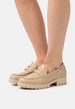 Mocassins en cuir beige avec un bout arrondi, une couture minimale et une semelle texturée, dotés d'un petit talon bloc pour la stabilité.
