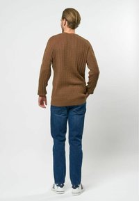 Pull marron tricoté avec une texture côtelée, col rond et manches longues, associé à un jean bleu et des baskets blanches.