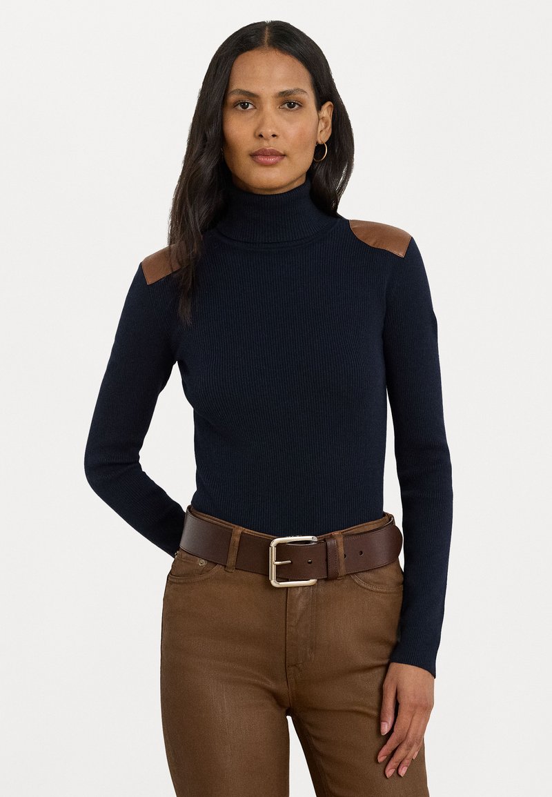 Pull en maille côtelée bleu marine avec des accents d'épaule en cuir marron ; associé à une ceinture et un pantalon marron. Texture lisse, design ajusté.