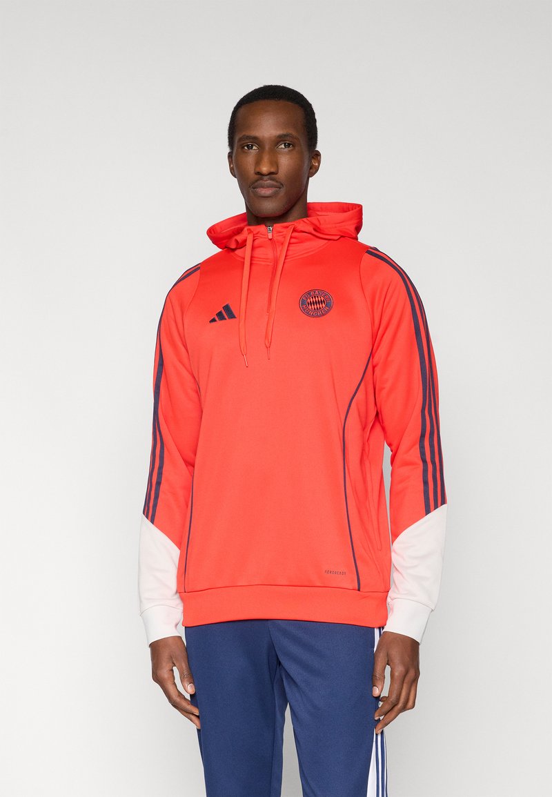 Sweat à capuche de sport rouge avec des rayures bleu marine, logo de la marque sur la poitrine, capuche ajustable et accents blancs sur les manches. Tissu doux et léger.