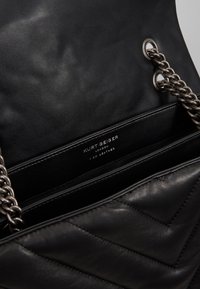 Czarna skórzana torebka z pikowanym wzorem, srebrnym łańcuchem na ramię i wytłoczonym logo w środku, z dwoma przegródkami.