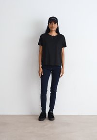 T-shirt en coton noir à manches courtes, associé à un jean skinny bleu foncé et des chaussures à plateforme noires. Une casquette noire complète la tenue.