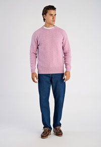 Ljusrosa kabelstickad tröja med ribbad krage och muddar, kombinerad med mörkblå jeans med raka ben och bruna båtskor.