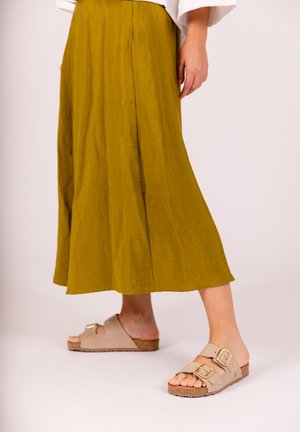 Olijfgroen rok met plooi, gecombineerd met beige instapsandalen met dubbele gespaccents en een gestructureerde zool.