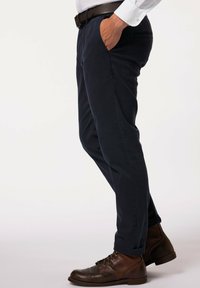 Chino navy in tessuto di cotone, con vestibilità rilassata, tasche laterali e orli arrotolati, abbinati a stivali in pelle marrone.