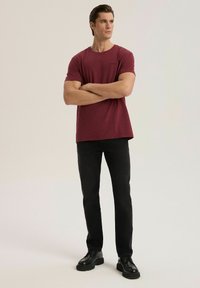 Bordowa koszulka z okrągłym dekoltem wykonana z teksturowanej tkaniny, zestawiona z czarnymi spodniami o prostych nogawkach i czarnymi sznurowanymi butami. Prosty design.