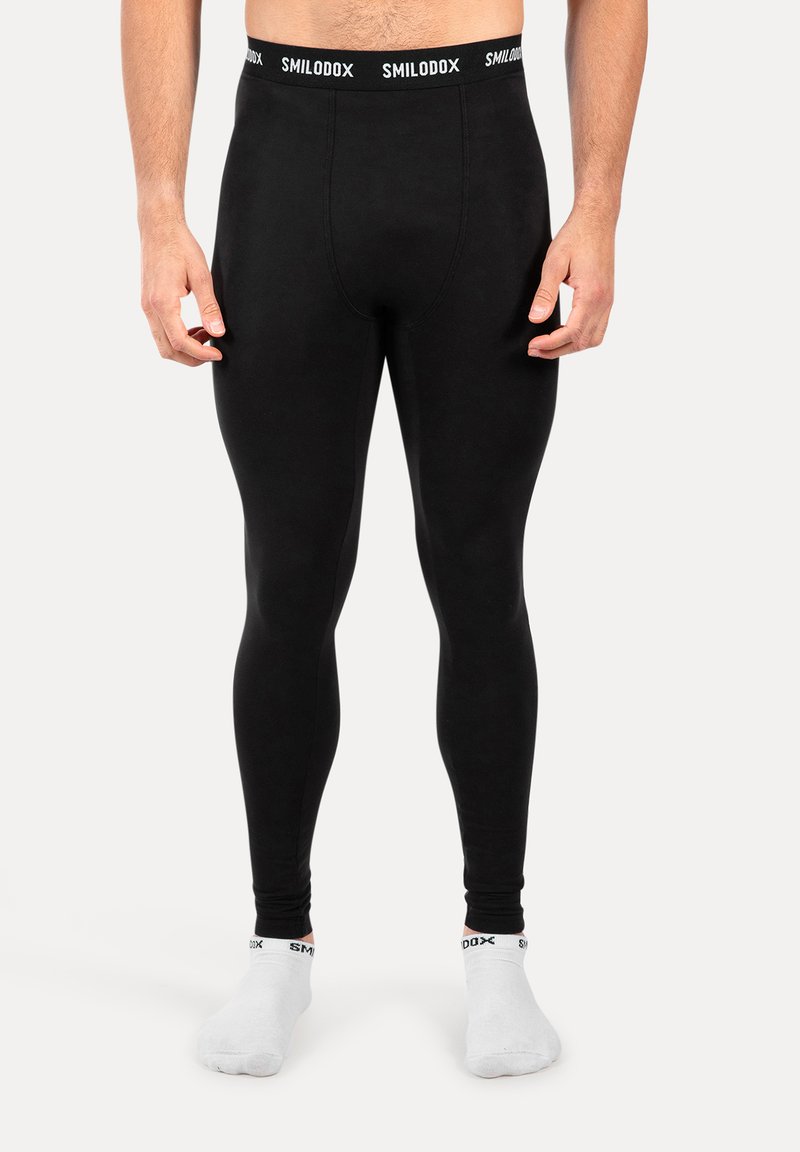 Hombre que lleva mallas térmicas ajustadas negras y calcetines tobilleros blancos con bandas elásticas de marca visibles.