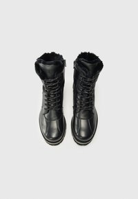 Botas de cuero negras con forro de piel, que presentan cordones y una cremallera, exhibidas desde arriba sobre un fondo blanco.