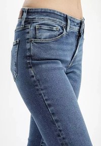 Dżinsy w średnim niebieskim kolorze, z klasycznym pięciokieszeniowym wzorem, lekkim wyblaknięciem oraz średnim stanem w pasie z skórzaną metką na tyle.