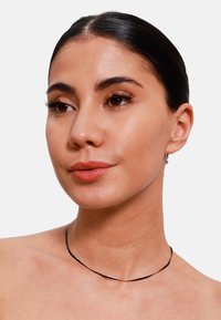 Choker noir fin en matériau flexible, avec un design courbé simple reposant délicatement sur le cou. Style lisse et minimaliste.