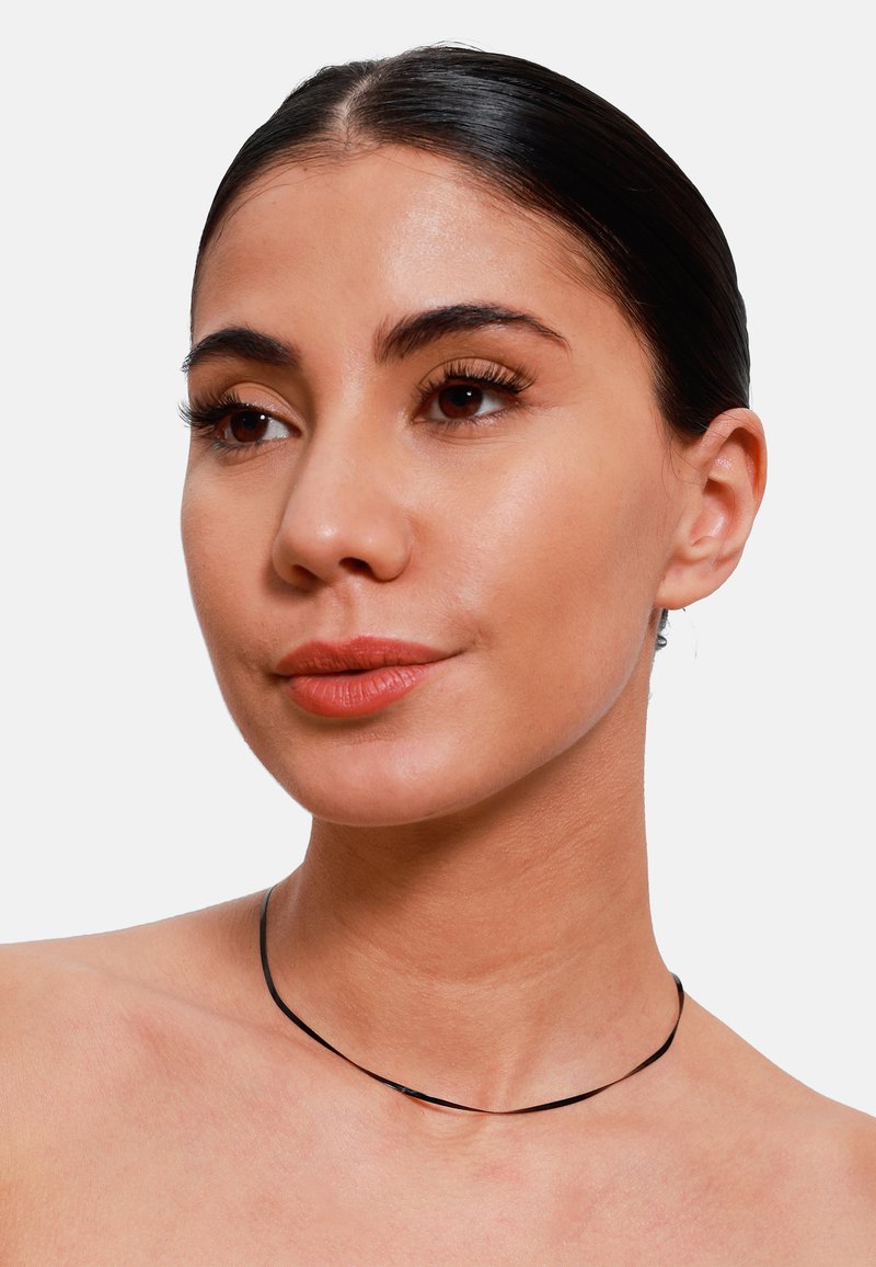 Choker noir fin en matériau flexible, avec un design courbé simple reposant délicatement sur le cou. Style lisse et minimaliste.