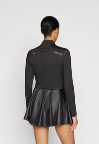 Tricou negru cu mâneci lungi, design cropped și panouri din material transparent pe spate, asortat cu o fustă neagră din piele ecologică, conică. Textură netedă în întregime.