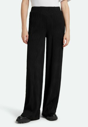 Black wide-leg pants with a textured ripple pattern and elastic waistband, paired with black platform shoes. Smooth fabric, casual design.