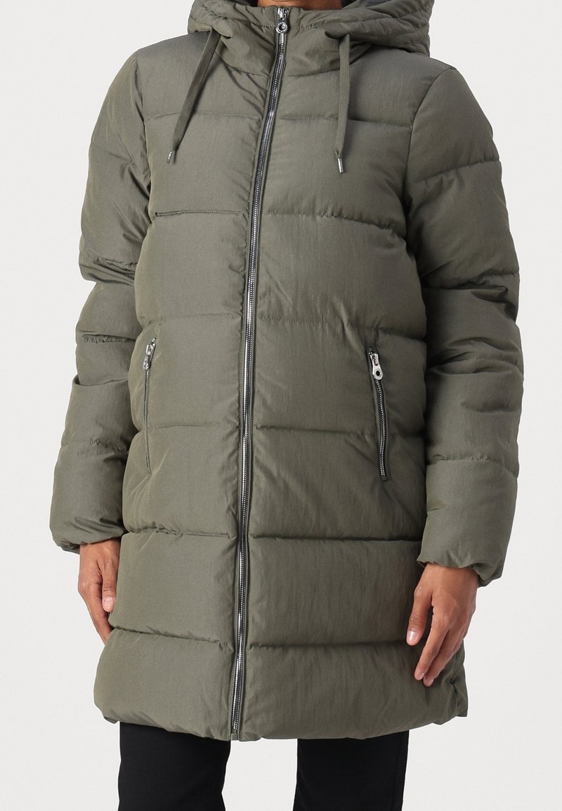 Parka acolchada de color verde oliva con cierre de cremallera, capucha ajustable y bolsillos laterales. Presenta una textura acolchada y un diseño hasta la rodilla.