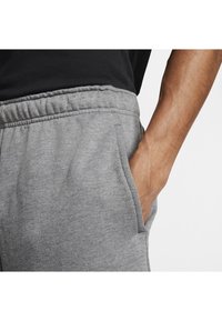 Grijze sweatpants met een elastische tailleband, zijzakken en een zachte stof; gedragen met een zwart shirt, met een hand in de zak.