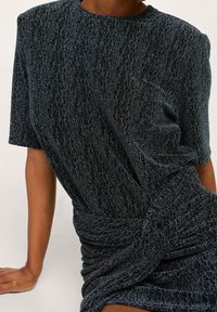 Abito lavorato a maglia scuro con una finitura testurizzata e brillante. Le maniche corte e un dettaglio attorcigliato in vita creano una silhouette aderente.