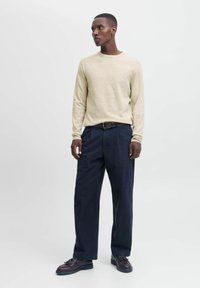 Beige Langarmpullover, marineblaue weite Hose, dunkle Schuhe. Einfaches Design, weicher Stoff und lockere Passform. Minimalistischer Stil.