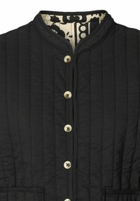 Veste matelassée noire avec col mandarin, cinq boutons beiges sur le devant et une doublure intérieure à motifs noir et blanc.