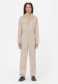 Mono beige de manga larga, con dos bolsillos en el pecho y un bolsillo lateral. Fabricado en tela duradera, con botones de presión y una cintura ajustada.