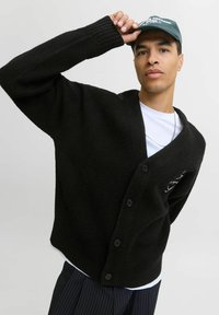 Schwarzer Wollmischungs-Cardigan mit V-Ausschnitt, langen Ärmeln und sechs Knöpfen. Er hat eine strukturierte Oberfläche und ein grafisches Detail auf der linken Brust.