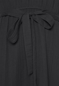 Vestido negro de tela con un diseño texturizado, con un lazo en la cintura y detalles fruncidos. El material parece suave y ligero.