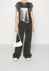 Metallisk grå topp med korta ärmar, i kombination med vida mörkgrå byxor. Håller en liten vit handväska med metallisk detalj. Vita skor.