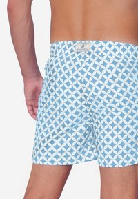 Costume de baie bleu deschis cu un model circular alb, talie elastică și buzunar la spate, fabricat dintr-un material neted, care se usucă rapid.