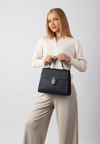 Black leather handbag with a structured design, gold hardware clasp, and top handle, set against a light background.