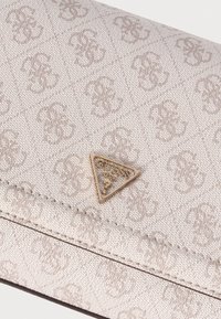 Beige portemonnee met geperst monogrampatroon, voorzien van een driehoekig gouden hardware-logo; gladde textuur en gestikte details.