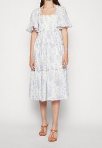 Midi sukienka w kwiatowy wzór w jasnoniebieskim i białym kolorze, z kwadratowym dekoltem, falbaniastymi rękawami i warstwową spódnicą. Uzupełniona o pomarańczowe sandały na paski.