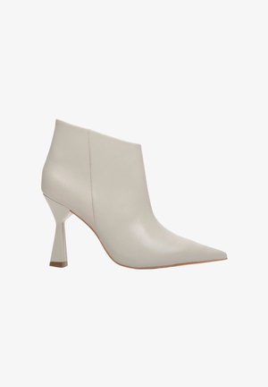 Beżowe skórzane botki za kostkę z ostrym noskiem i unikalnym kanciastym obcasem. Gładka tekstura z minimalnymi detalami przeszyć i elegancki kształt.
