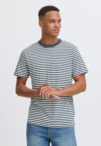 Juostuota marškinėliai su tamsiai mėlynomis ir kreminėmis horizontaliomis juostelėmis, apvaliu kaklu, trumpomis rankovėmis, minkšta medžiaga ir laisvas fasonas. Dėvimi su šviesiai mėlynomis džinsomis.