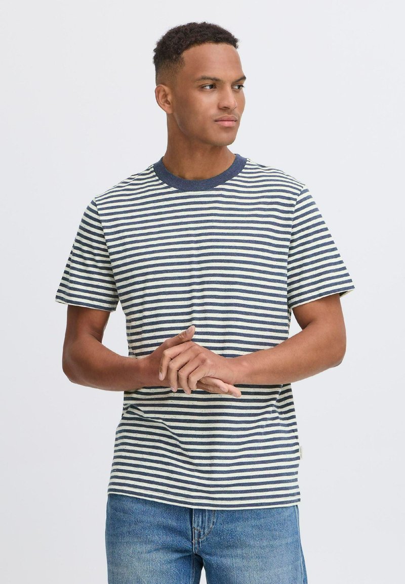 Juostuota marškinėliai su tamsiai mėlynomis ir kreminėmis horizontaliomis juostelėmis, apvaliu kaklu, trumpomis rankovėmis, minkšta medžiaga ir laisvas fasonas. Dėvimi su šviesiai mėlynomis džinsomis.