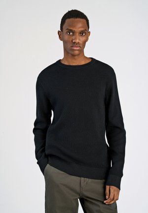 Black ribbed sweater with a round neckline and long sleeves, paired with olive green pants. The fabric appears textured and fitted.