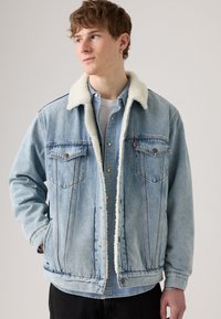 Light blue denim jacket with a white faux shearling collar, two chest pockets, snap buttons, and a relaxed fit. Textured fabric appears worn.